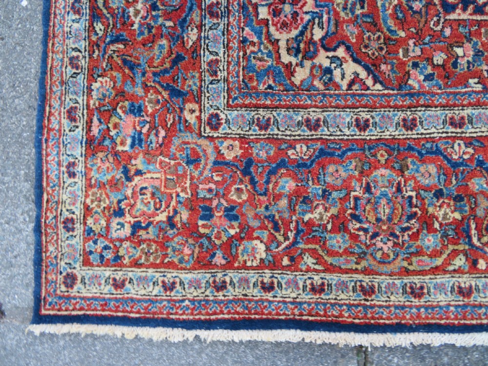 An antique hand-knotted Persian Kashan wool rug featuring a central ivory and red medallion surrounded by dense floral motifs on a dark blue field. View XIII