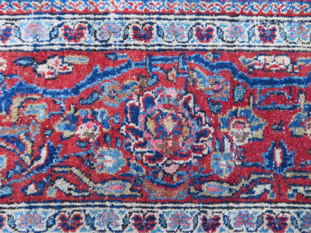 An antique hand-knotted Persian Kashan wool rug featuring a central ivory and red medallion surrounded by dense floral motifs on a dark blue field. View XIX