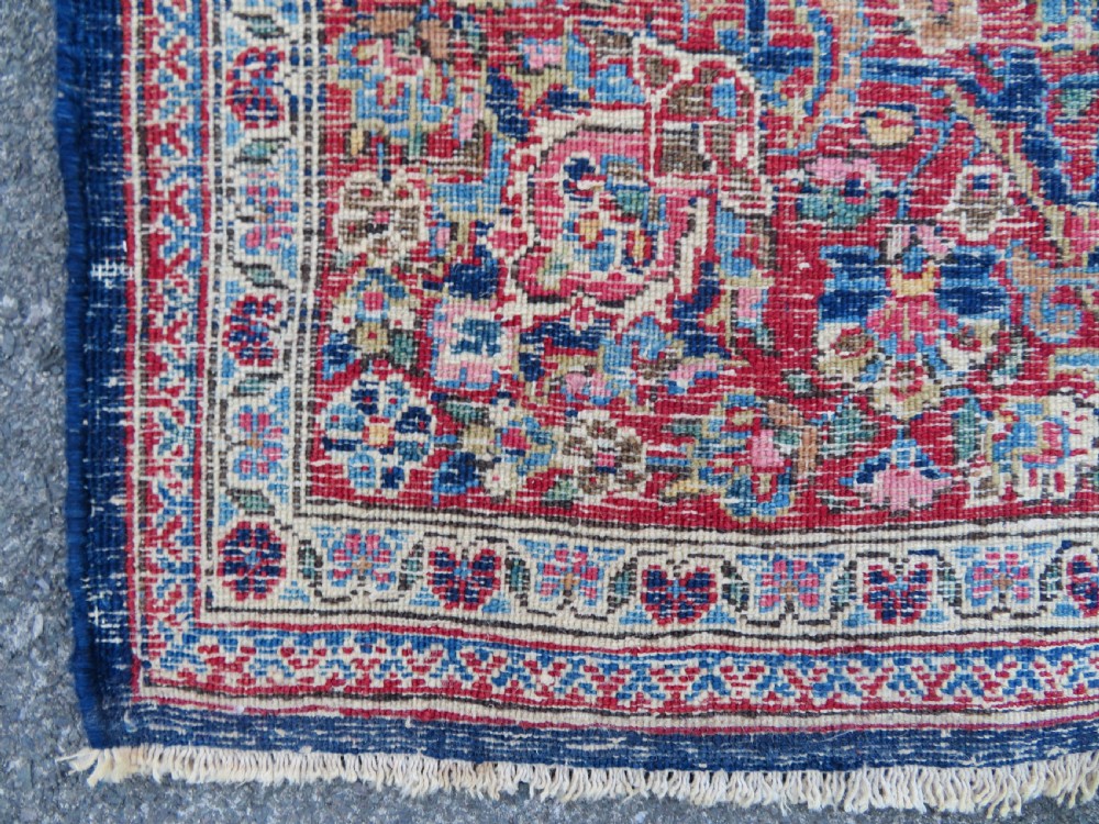 An antique hand-knotted Persian Kashan wool rug featuring a central ivory and red medallion surrounded by dense floral motifs on a dark blue field. View XXI
