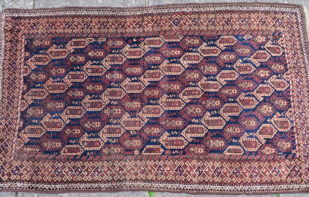 A hand-knotted antique Baluch rug featuring repeating geometric octagonal motifs in shades of dark blue, terracotta, and brown framed by patterned geometric borders. View III