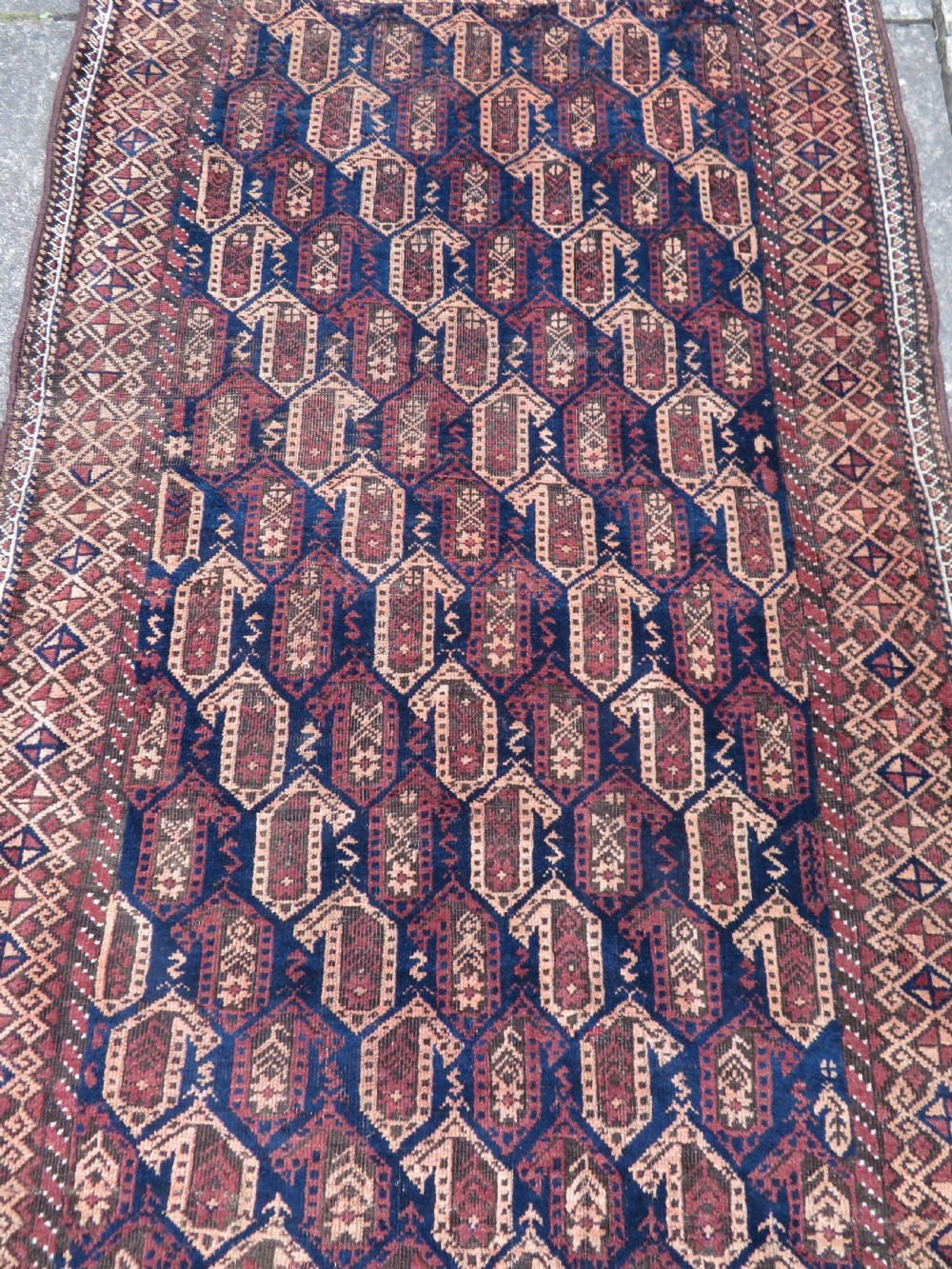 A hand-knotted antique Baluch rug featuring repeating geometric octagonal motifs in shades of dark blue, terracotta, and brown framed by patterned geometric borders. View IV