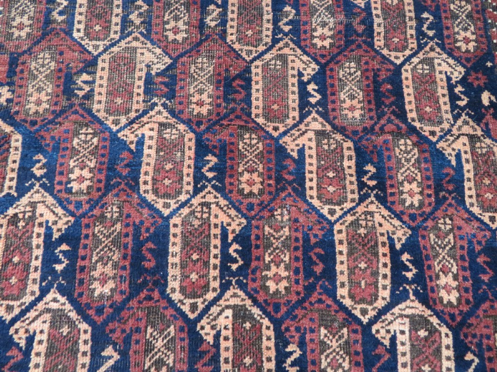 A hand-knotted antique Baluch rug featuring repeating geometric octagonal motifs in shades of dark blue, terracotta, and brown framed by patterned geometric borders. View V