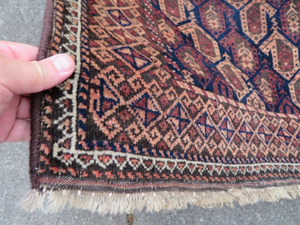 A hand-knotted antique Baluch rug featuring repeating geometric octagonal motifs in shades of dark blue, terracotta, and brown framed by patterned geometric borders. View VIII