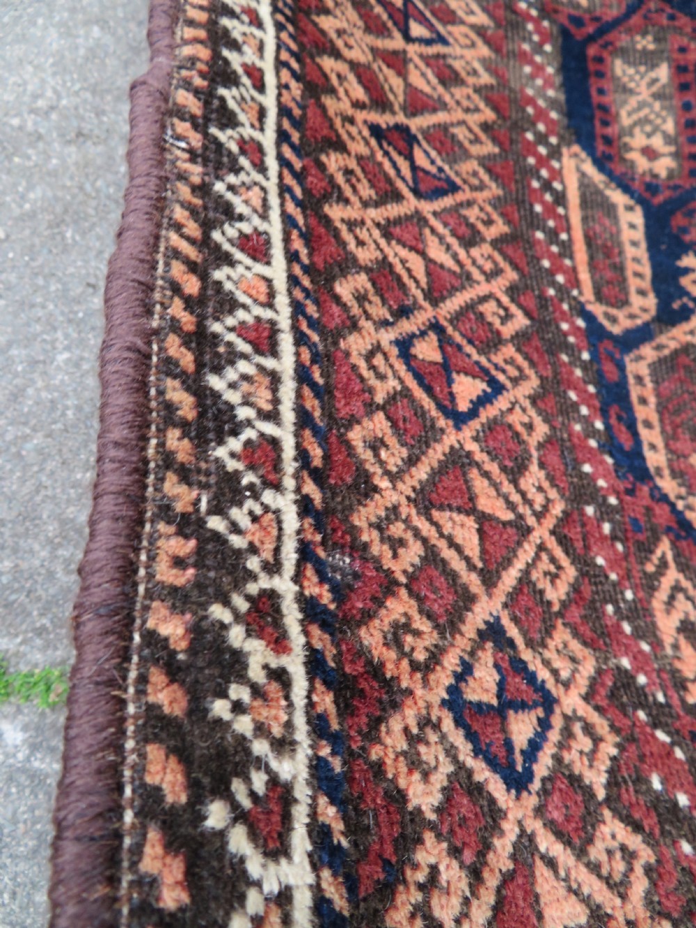 A hand-knotted antique Baluch rug featuring repeating geometric octagonal motifs in shades of dark blue, terracotta, and brown framed by patterned geometric borders. View X