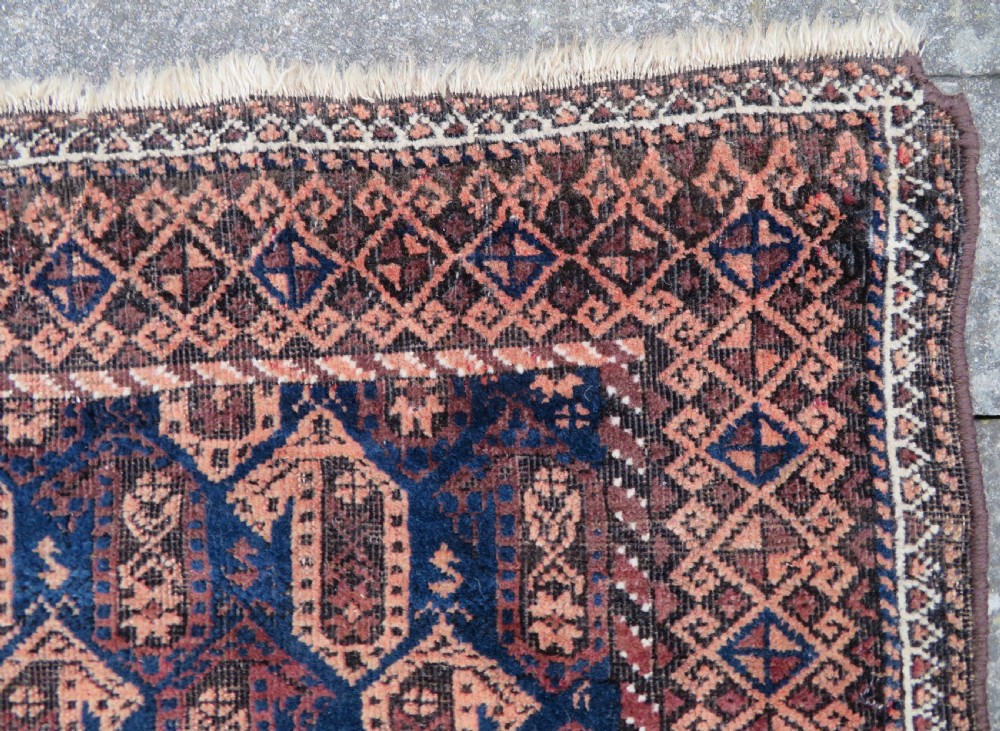 A hand-knotted antique Baluch rug featuring repeating geometric octagonal motifs in shades of dark blue, terracotta, and brown framed by patterned geometric borders. View XI