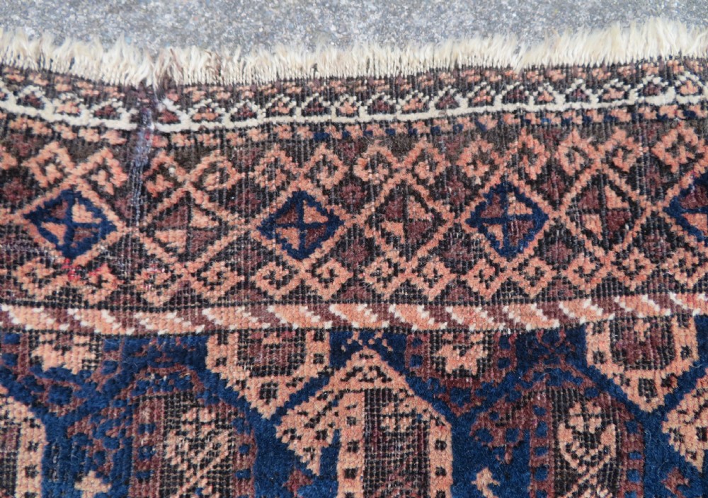 A hand-knotted antique Baluch rug featuring repeating geometric octagonal motifs in shades of dark blue, terracotta, and brown framed by patterned geometric borders. View XII