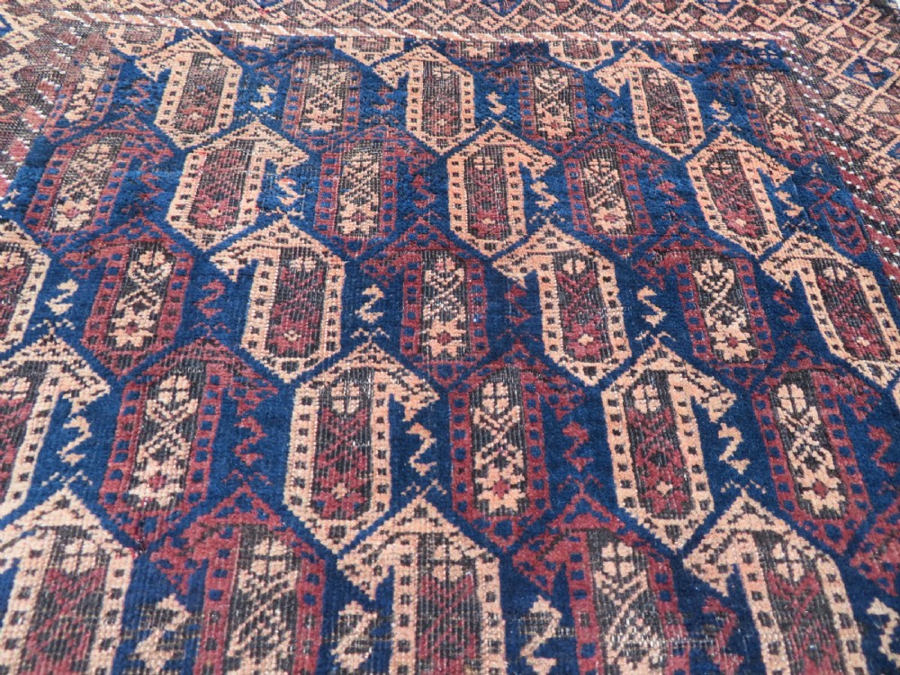 A hand-knotted antique Baluch rug featuring repeating geometric octagonal motifs in shades of dark blue, terracotta, and brown framed by patterned geometric borders. View XIII