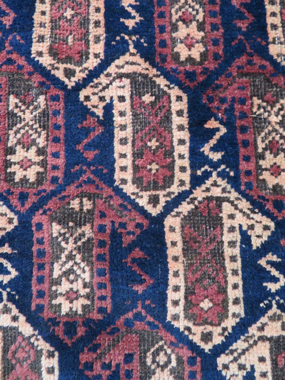 A hand-knotted antique Baluch rug featuring repeating geometric octagonal motifs in shades of dark blue, terracotta, and brown framed by patterned geometric borders. View XIV