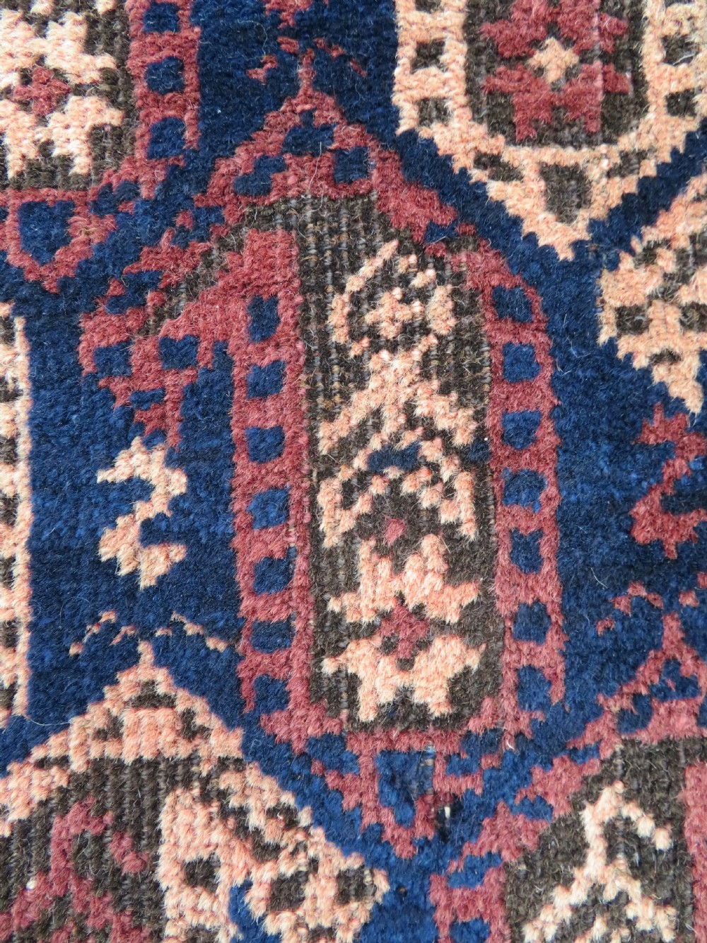 A hand-knotted antique Baluch rug featuring repeating geometric octagonal motifs in shades of dark blue, terracotta, and brown framed by patterned geometric borders. View XV