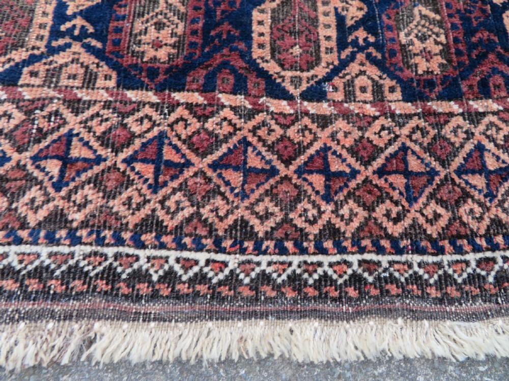 A hand-knotted antique Baluch rug featuring repeating geometric octagonal motifs in shades of dark blue, terracotta, and brown framed by patterned geometric borders. View XVI