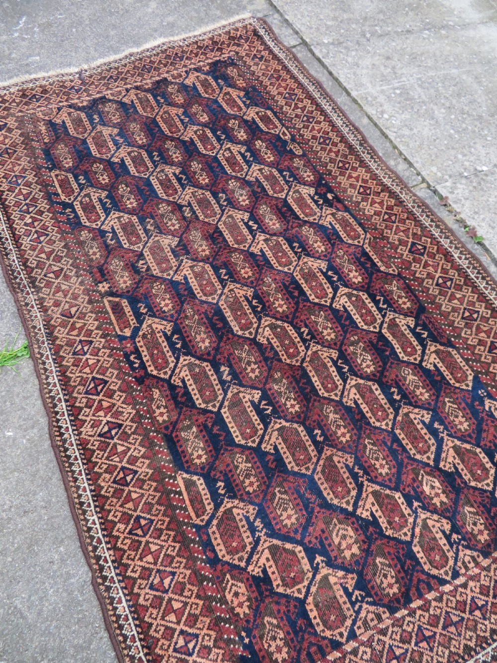 A hand-knotted antique Baluch rug featuring repeating geometric octagonal motifs in shades of dark blue, terracotta, and brown framed by patterned geometric borders. View XVII