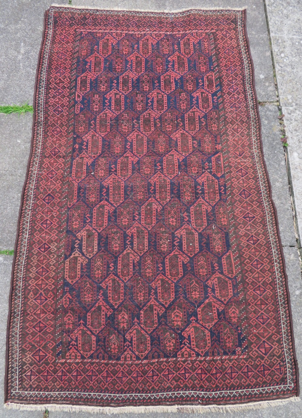 A hand-knotted antique Baluch rug featuring repeating geometric octagonal motifs in shades of dark blue, terracotta, and brown framed by patterned geometric borders. View XVIII