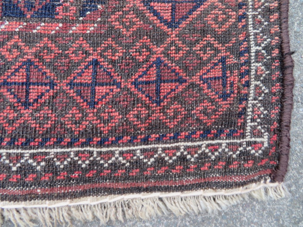 A hand-knotted antique Baluch rug featuring repeating geometric octagonal motifs in shades of dark blue, terracotta, and brown framed by patterned geometric borders. View XIX