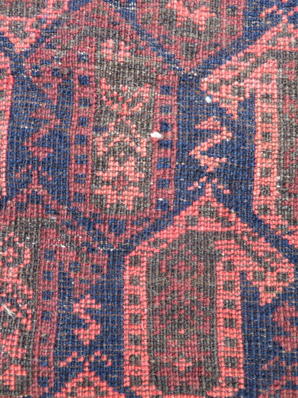 A hand-knotted antique Baluch rug featuring repeating geometric octagonal motifs in shades of dark blue, terracotta, and brown framed by patterned geometric borders. View XX