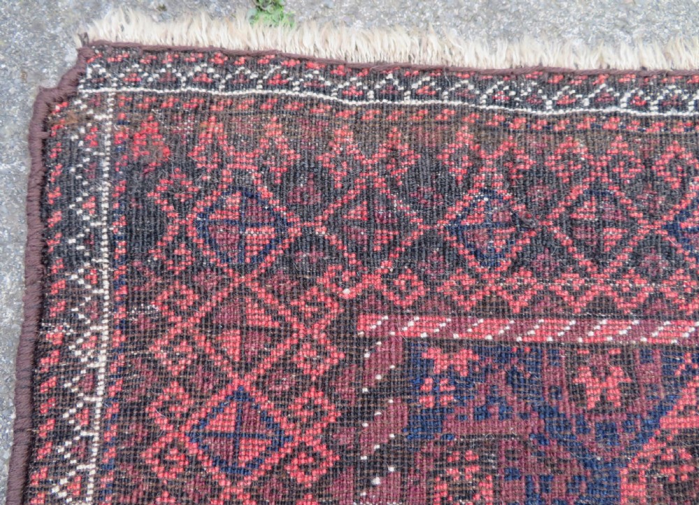 A hand-knotted antique Baluch rug featuring repeating geometric octagonal motifs in shades of dark blue, terracotta, and brown framed by patterned geometric borders. View XXI