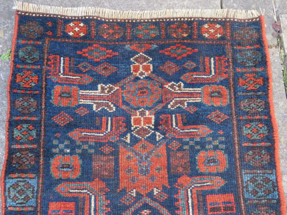 An antique Kurdish wool runner rug featuring geometric and stylized human figures in navy blue, madder red, and ochre with fringed ends. View III