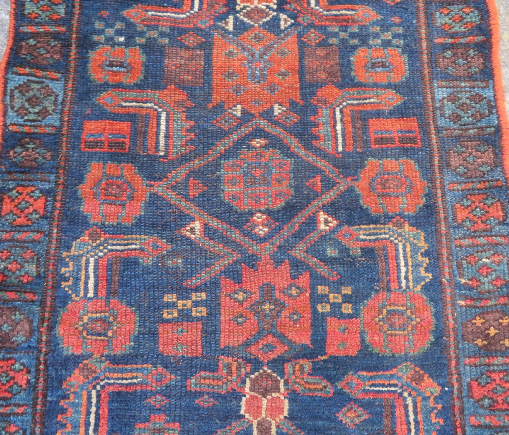 An antique Kurdish wool runner rug featuring geometric and stylized human figures in navy blue, madder red, and ochre with fringed ends. View IV