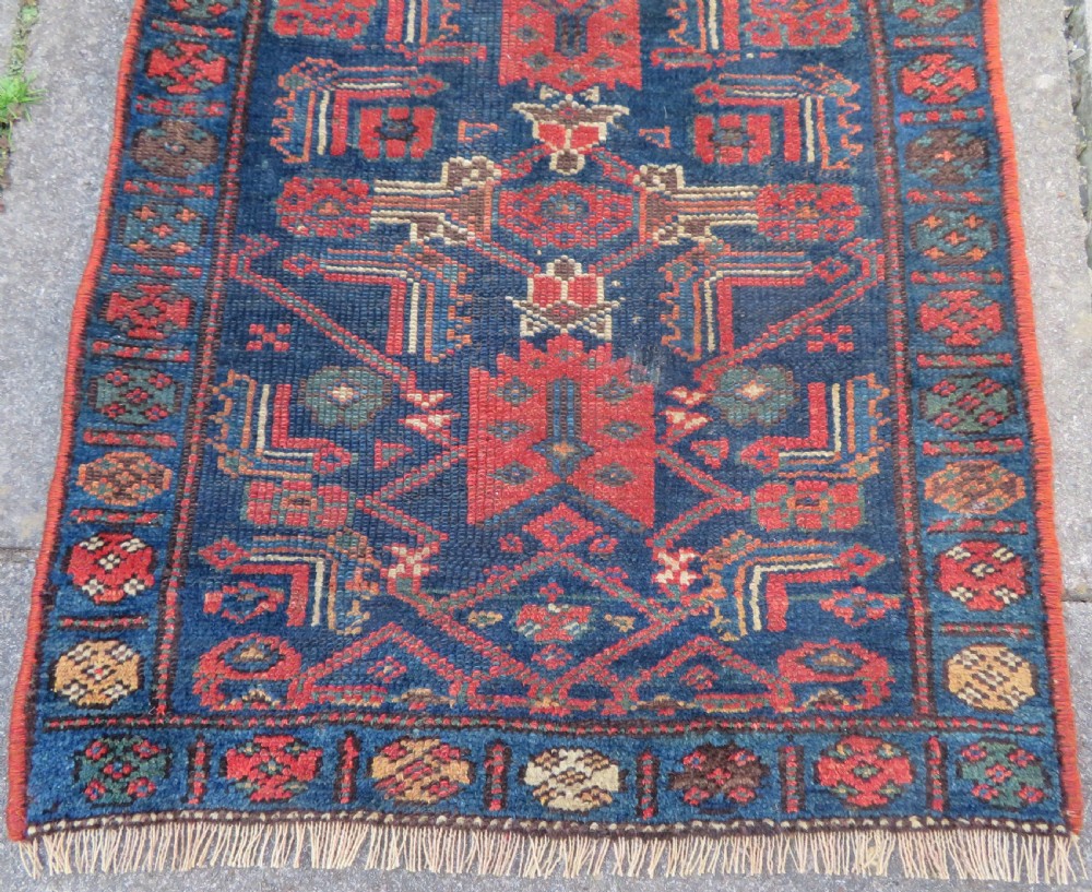 An antique Kurdish wool runner rug featuring geometric and stylized human figures in navy blue, madder red, and ochre with fringed ends. View VII