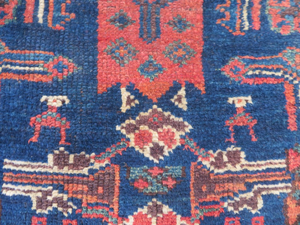 An antique Kurdish wool runner rug featuring geometric and stylized human figures in navy blue, madder red, and ochre with fringed ends. View VIII