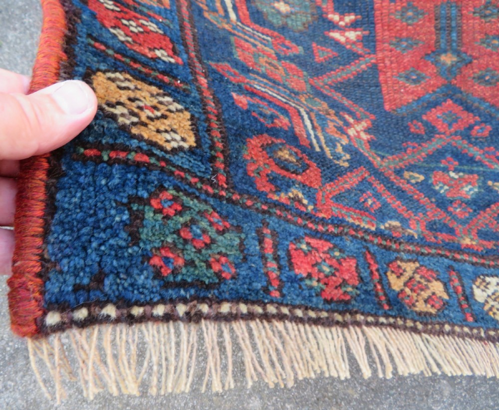 An antique Kurdish wool runner rug featuring geometric and stylized human figures in navy blue, madder red, and ochre with fringed ends. View XI