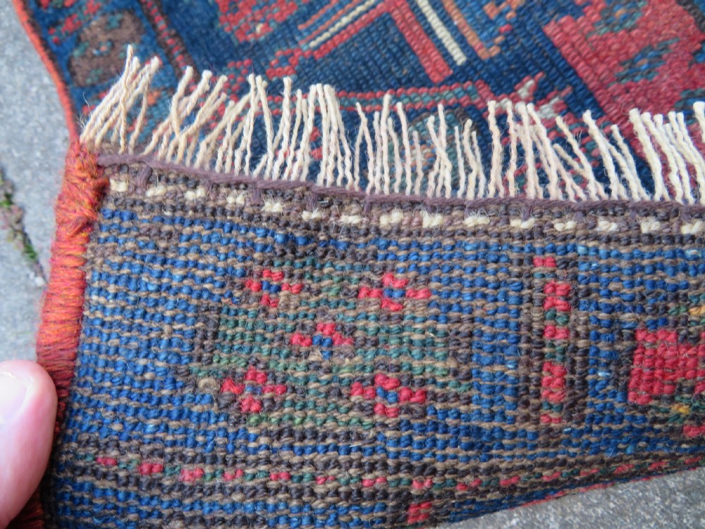 An antique Kurdish wool runner rug featuring geometric and stylized human figures in navy blue, madder red, and ochre with fringed ends. View XII