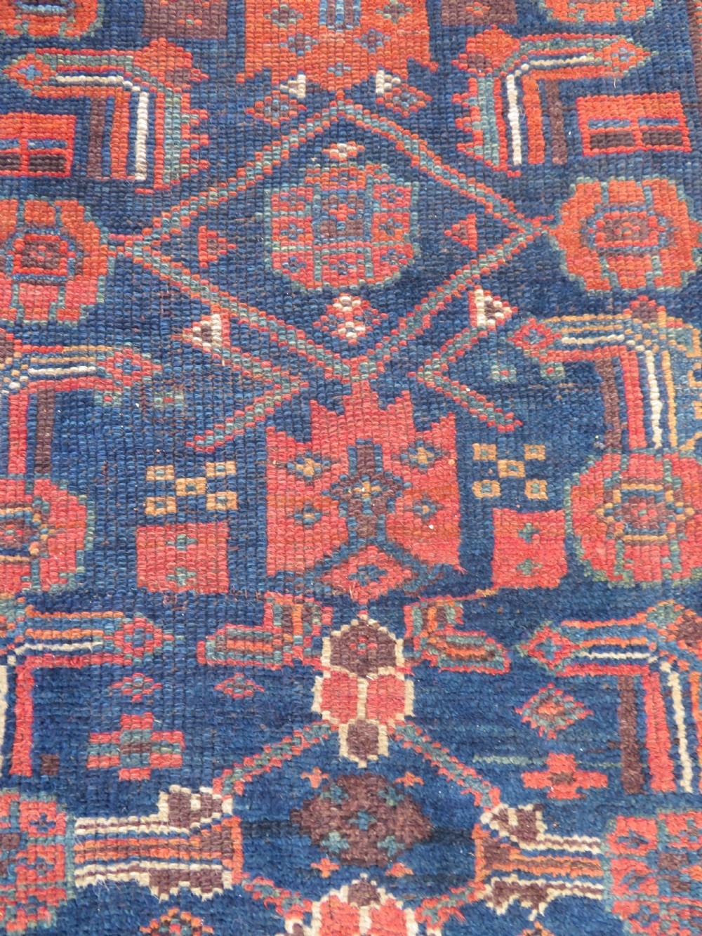 An antique Kurdish wool runner rug featuring geometric and stylized human figures in navy blue, madder red, and ochre with fringed ends. View XIII