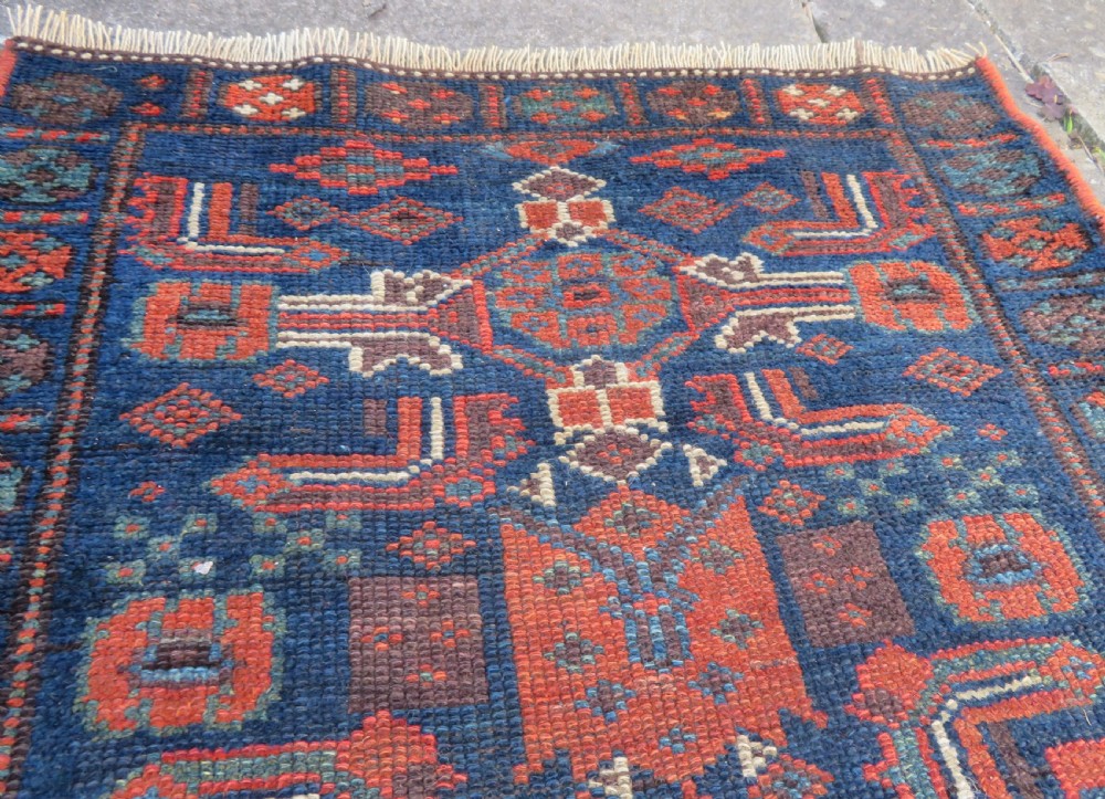An antique Kurdish wool runner rug featuring geometric and stylized human figures in navy blue, madder red, and ochre with fringed ends. View XIV