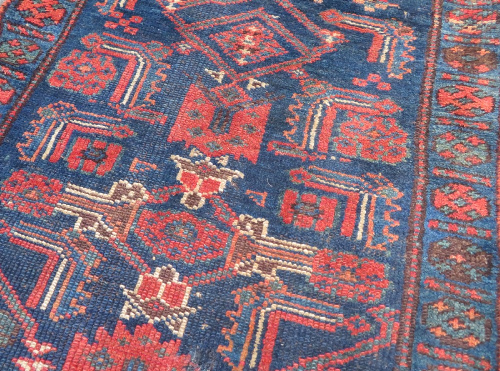 An antique Kurdish wool runner rug featuring geometric and stylized human figures in navy blue, madder red, and ochre with fringed ends. View XV