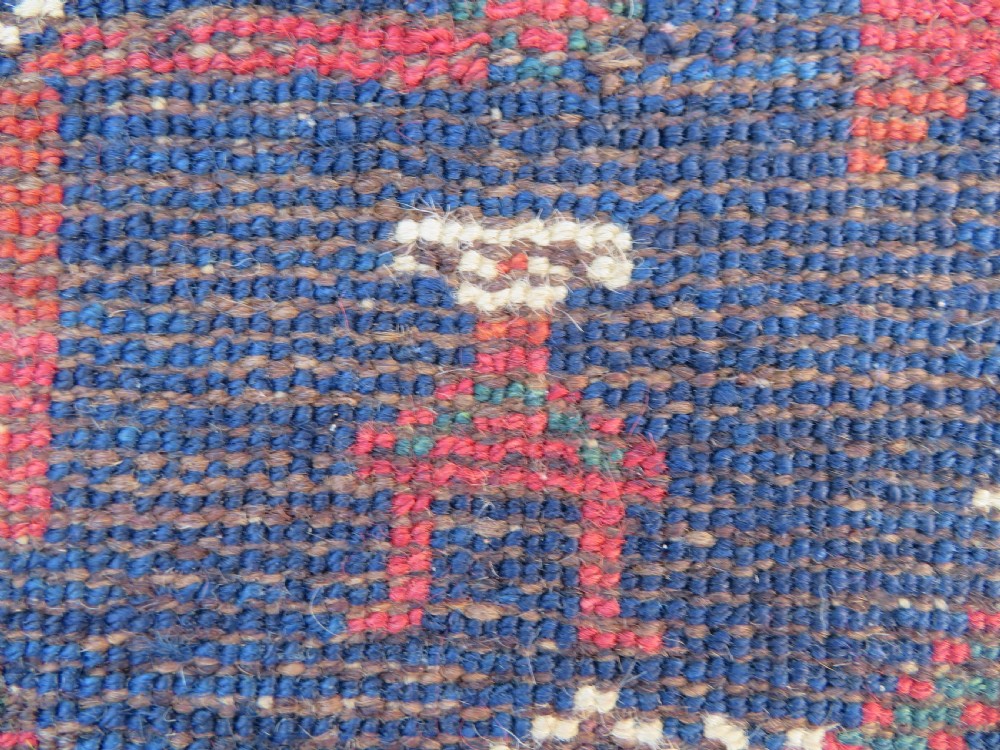 An antique Kurdish wool runner rug featuring geometric and stylized human figures in navy blue, madder red, and ochre with fringed ends. View XIX