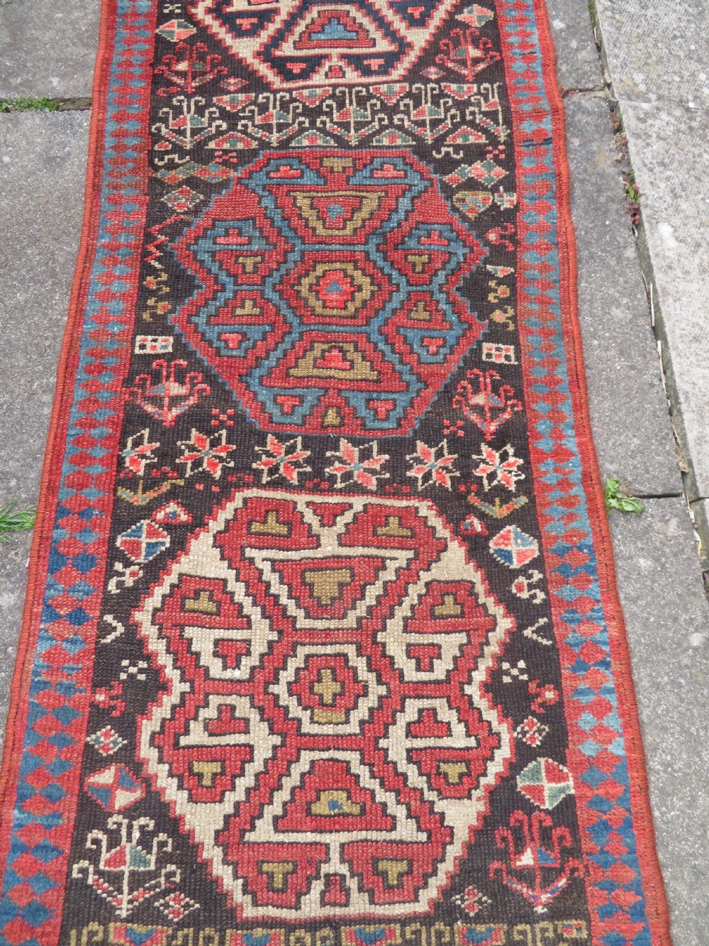 An antique hand-knotted Kurdish runner rug featuring five large geometric medallions in blue, red, and cream on a dark brown field. View IV