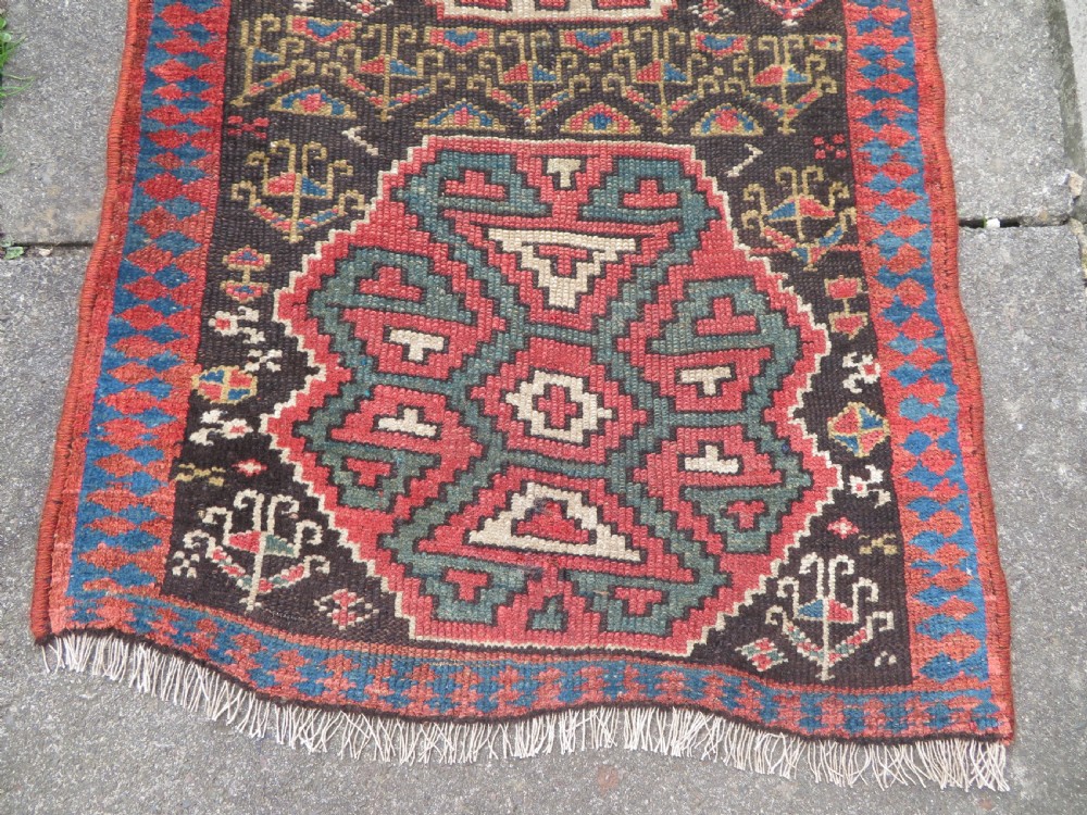 An antique hand-knotted Kurdish runner rug featuring five large geometric medallions in blue, red, and cream on a dark brown field. View V