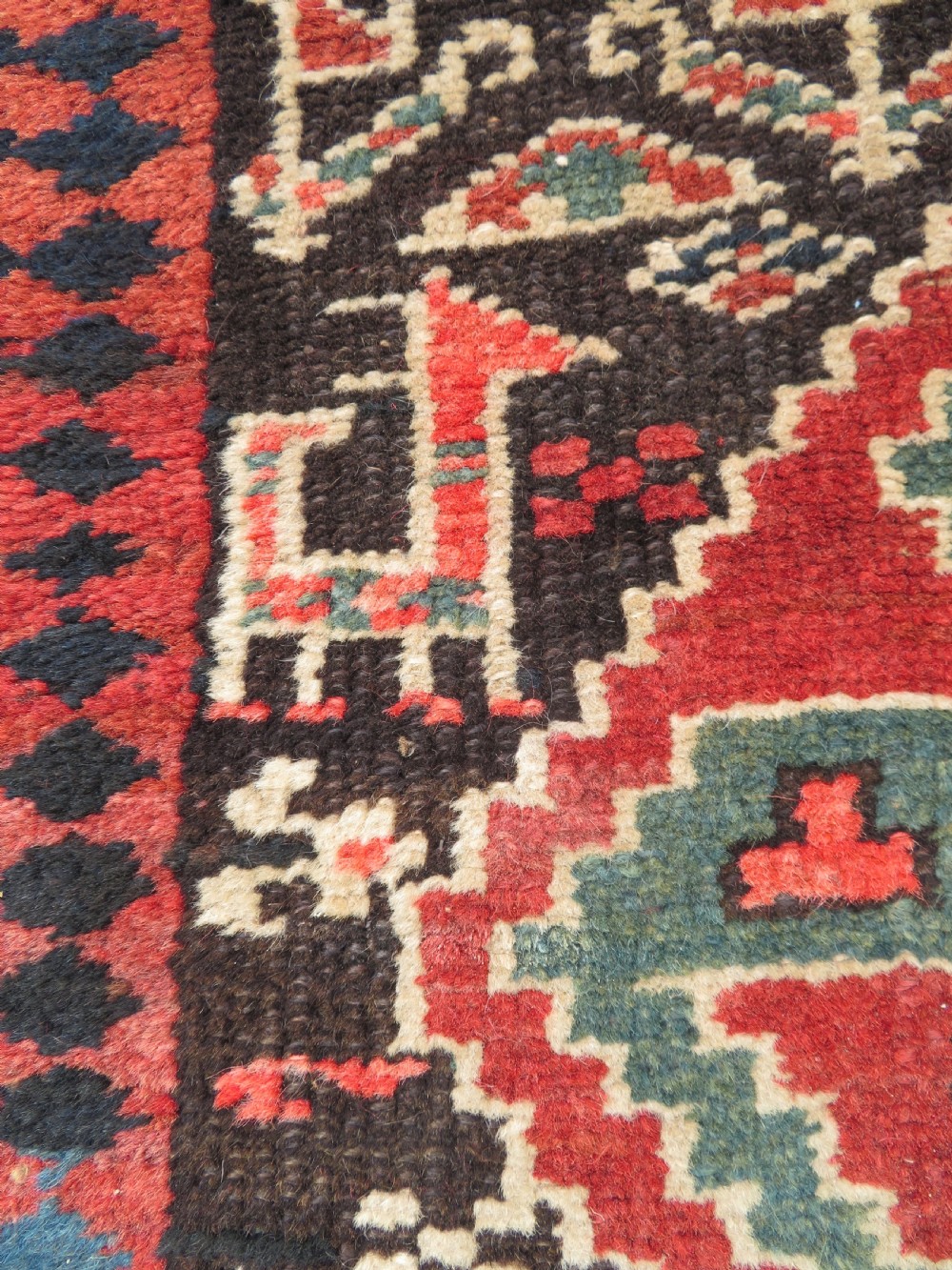 An antique hand-knotted Kurdish runner rug featuring five large geometric medallions in blue, red, and cream on a dark brown field. View VII