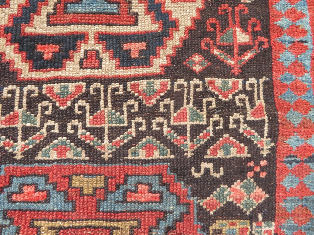 An antique hand-knotted Kurdish runner rug featuring five large geometric medallions in blue, red, and cream on a dark brown field. View XI