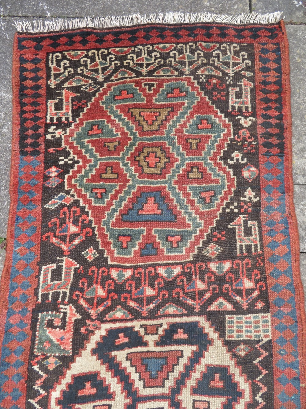 An antique hand-knotted Kurdish runner rug featuring five large geometric medallions in blue, red, and cream on a dark brown field. View III