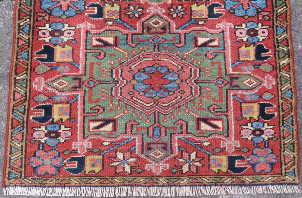 A long, narrow hand-knotted Persian Karaja wool rug runner featuring repeating geometric medallions in navy, blue, and cream against a rust red field. View III