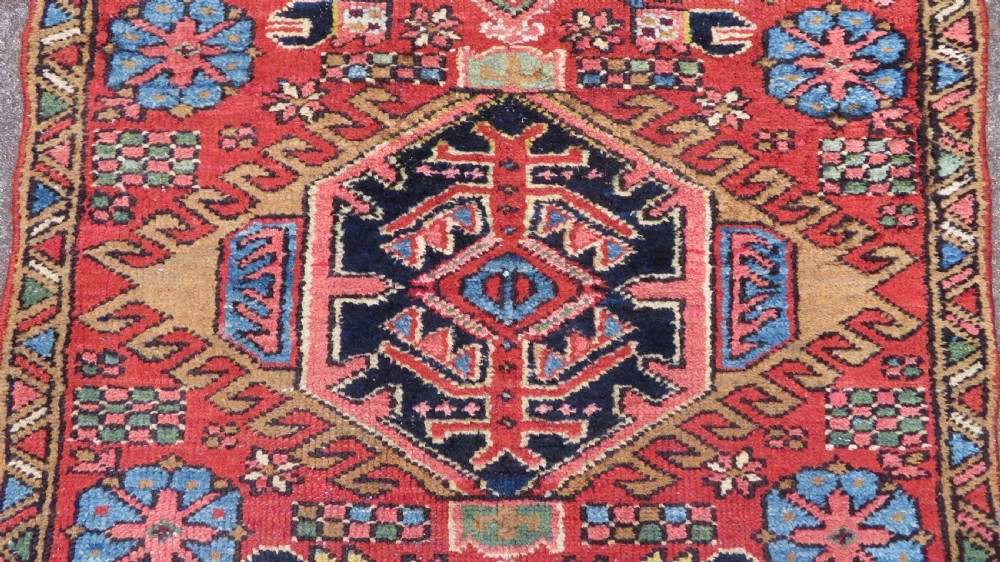 A long, narrow hand-knotted Persian Karaja wool rug runner featuring repeating geometric medallions in navy, blue, and cream against a rust red field. View IV