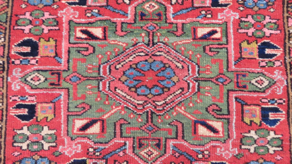 A long, narrow hand-knotted Persian Karaja wool rug runner featuring repeating geometric medallions in navy, blue, and cream against a rust red field. View V
