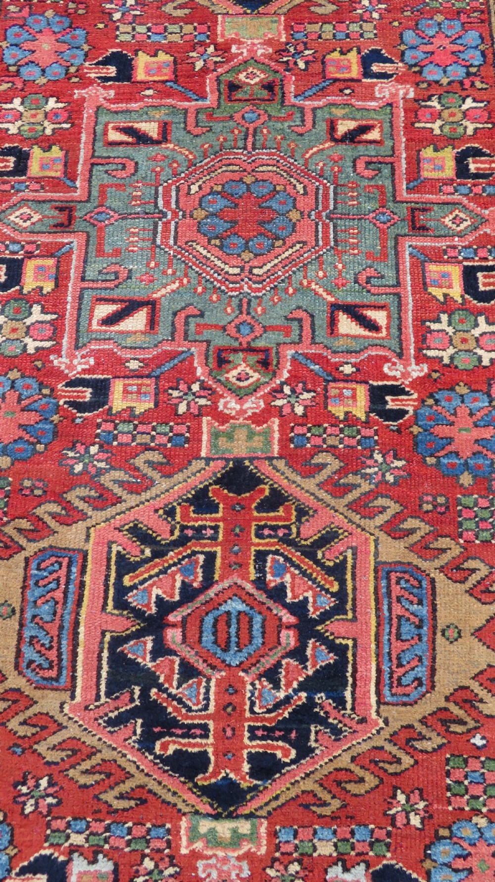 A long, narrow hand-knotted Persian Karaja wool rug runner featuring repeating geometric medallions in navy, blue, and cream against a rust red field. View VI