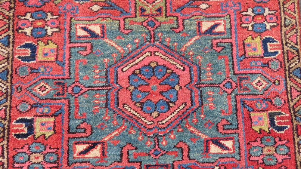 A long, narrow hand-knotted Persian Karaja wool rug runner featuring repeating geometric medallions in navy, blue, and cream against a rust red field. View VII