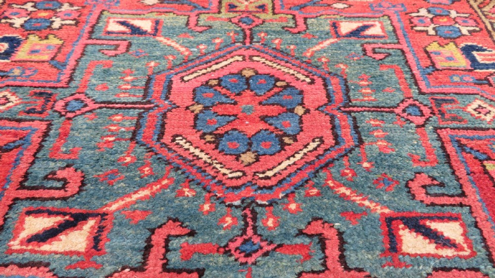A long, narrow hand-knotted Persian Karaja wool rug runner featuring repeating geometric medallions in navy, blue, and cream against a rust red field. View VIII