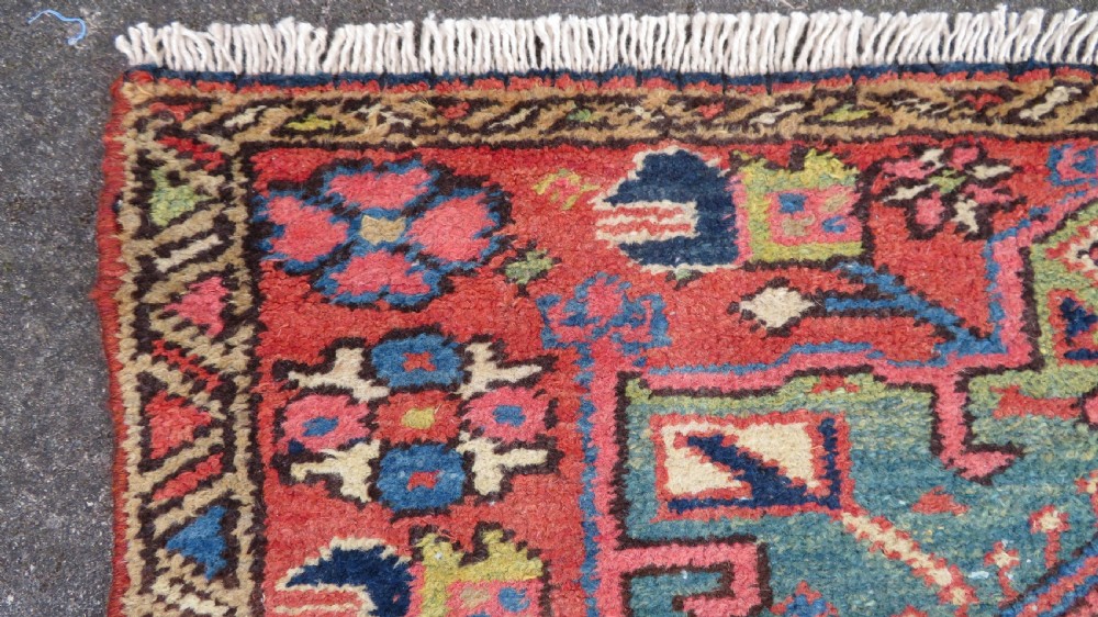 A long, narrow hand-knotted Persian Karaja wool rug runner featuring repeating geometric medallions in navy, blue, and cream against a rust red field. View XIII