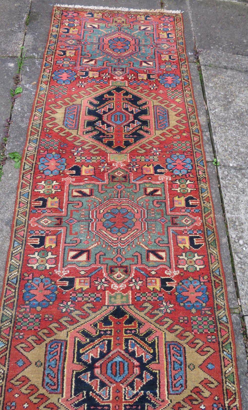 A long, narrow hand-knotted Persian Karaja wool rug runner featuring repeating geometric medallions in navy, blue, and cream against a rust red field. View XVI