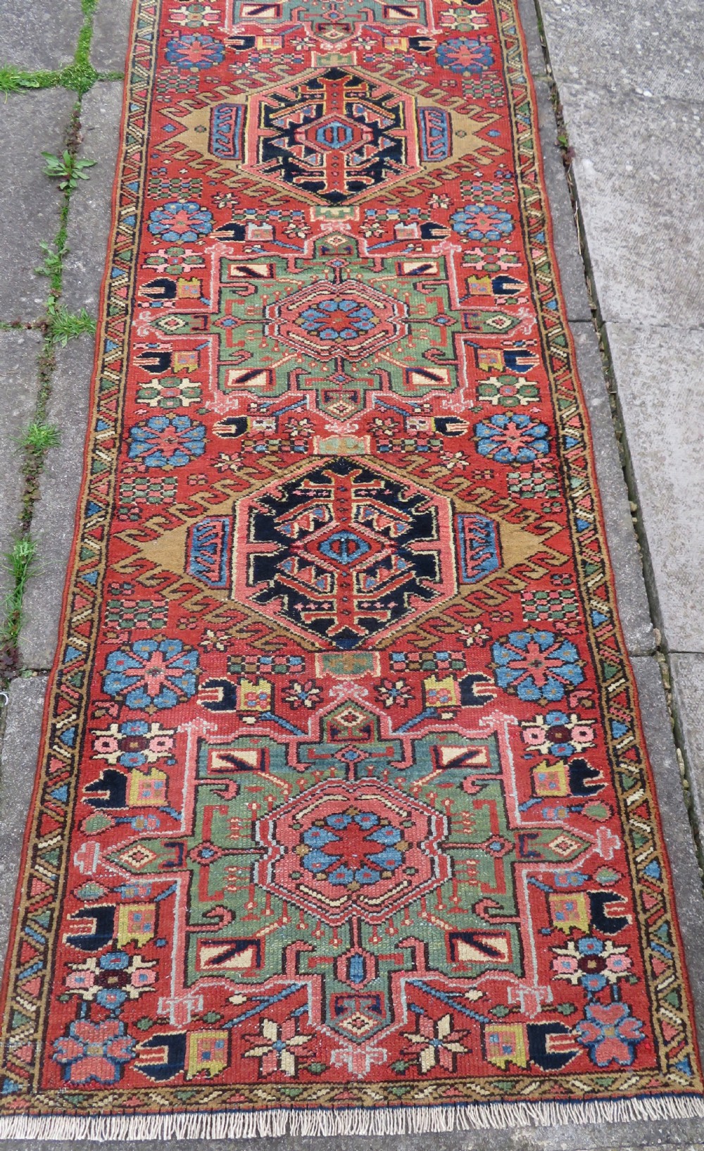 A long, narrow hand-knotted Persian Karaja wool rug runner featuring repeating geometric medallions in navy, blue, and cream against a rust red field. View XVII