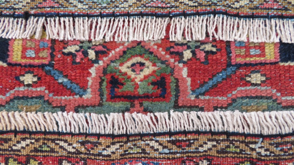 A long, narrow hand-knotted Persian Karaja wool rug runner featuring repeating geometric medallions in navy, blue, and cream against a rust red field. View XIX
