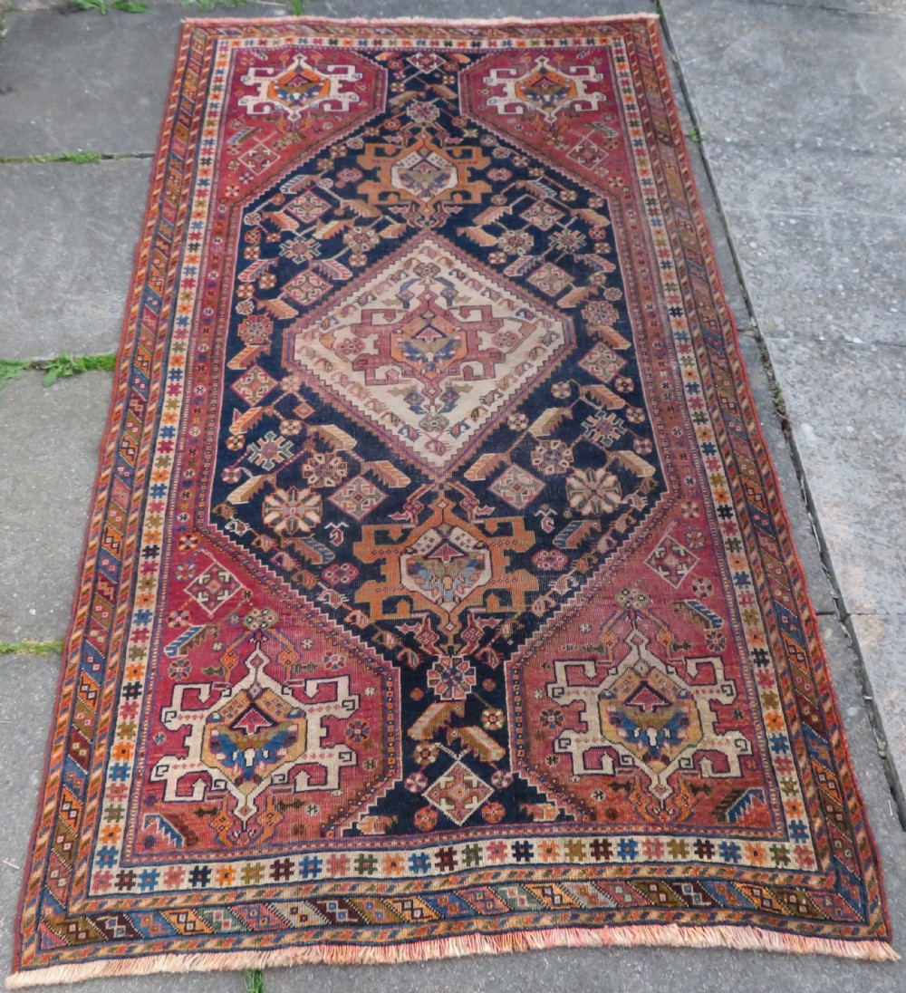 An antique Qashqai hand-knotted wool rug featuring a central diamond medallion surrounded by geometric tribal motifs in shades of navy blue, terracotta red, and cream. View II