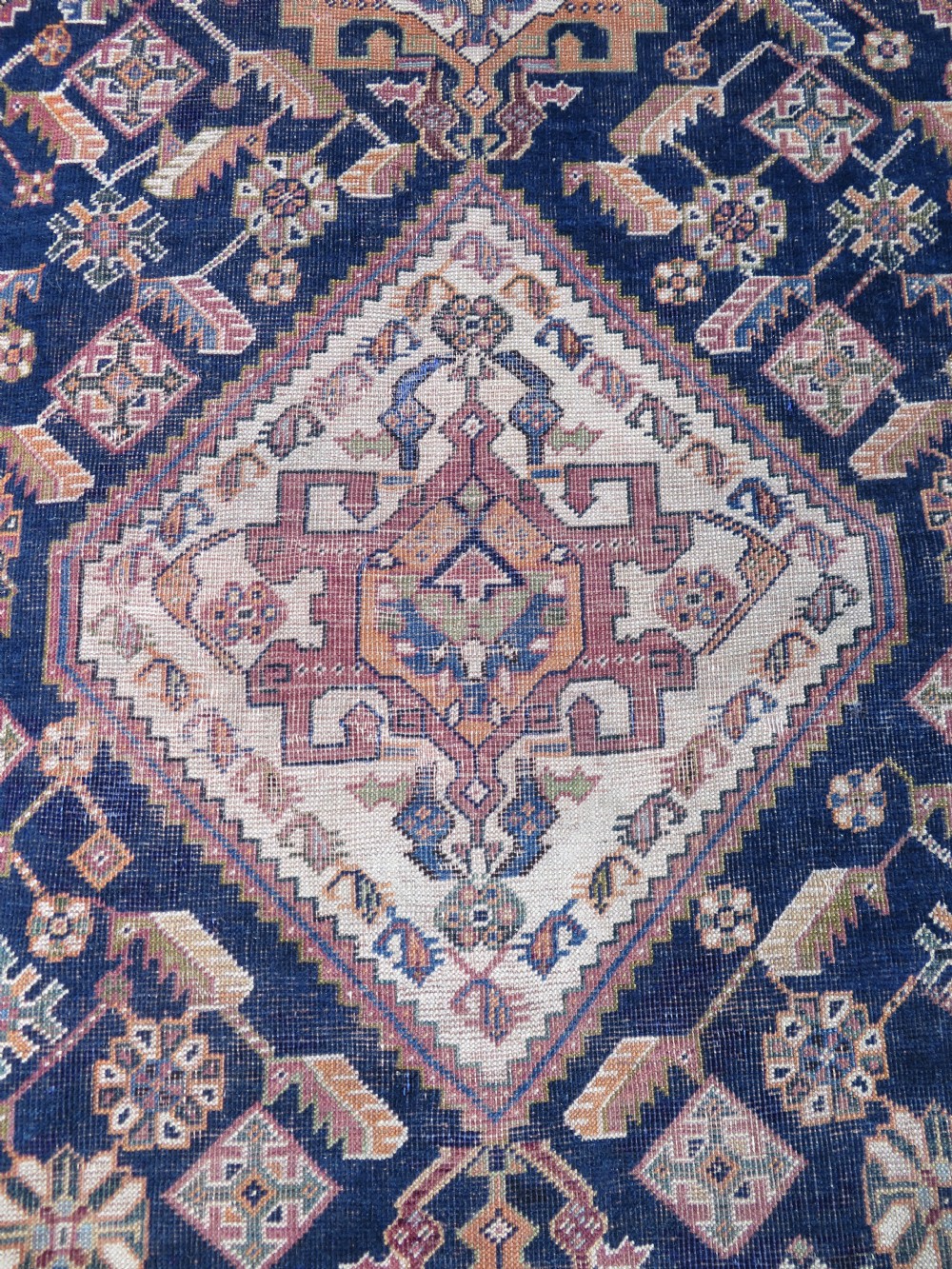 An antique Qashqai hand-knotted wool rug featuring a central diamond medallion surrounded by geometric tribal motifs in shades of navy blue, terracotta red, and cream. View III