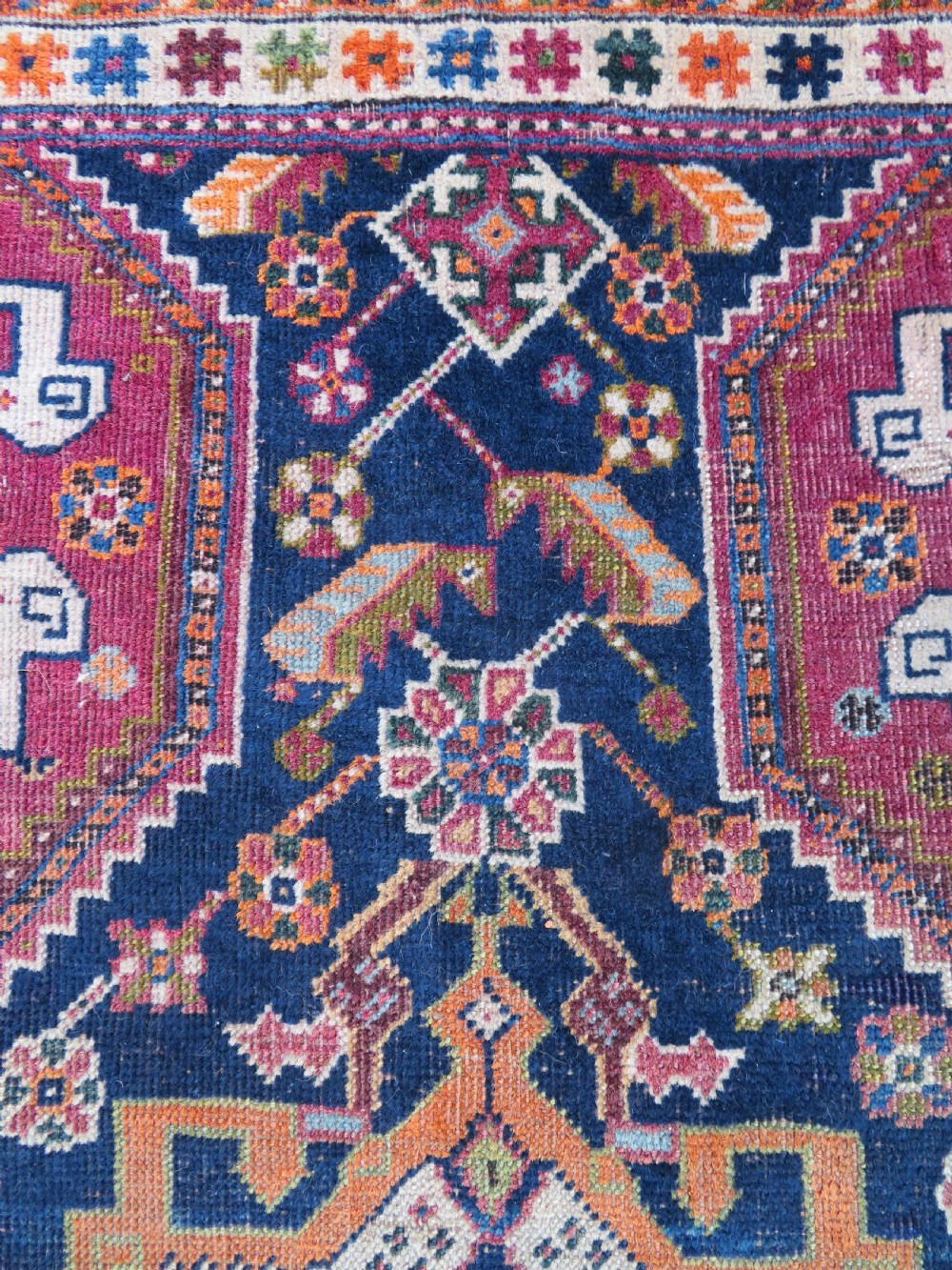 An antique Qashqai hand-knotted wool rug featuring a central diamond medallion surrounded by geometric tribal motifs in shades of navy blue, terracotta red, and cream. View VI