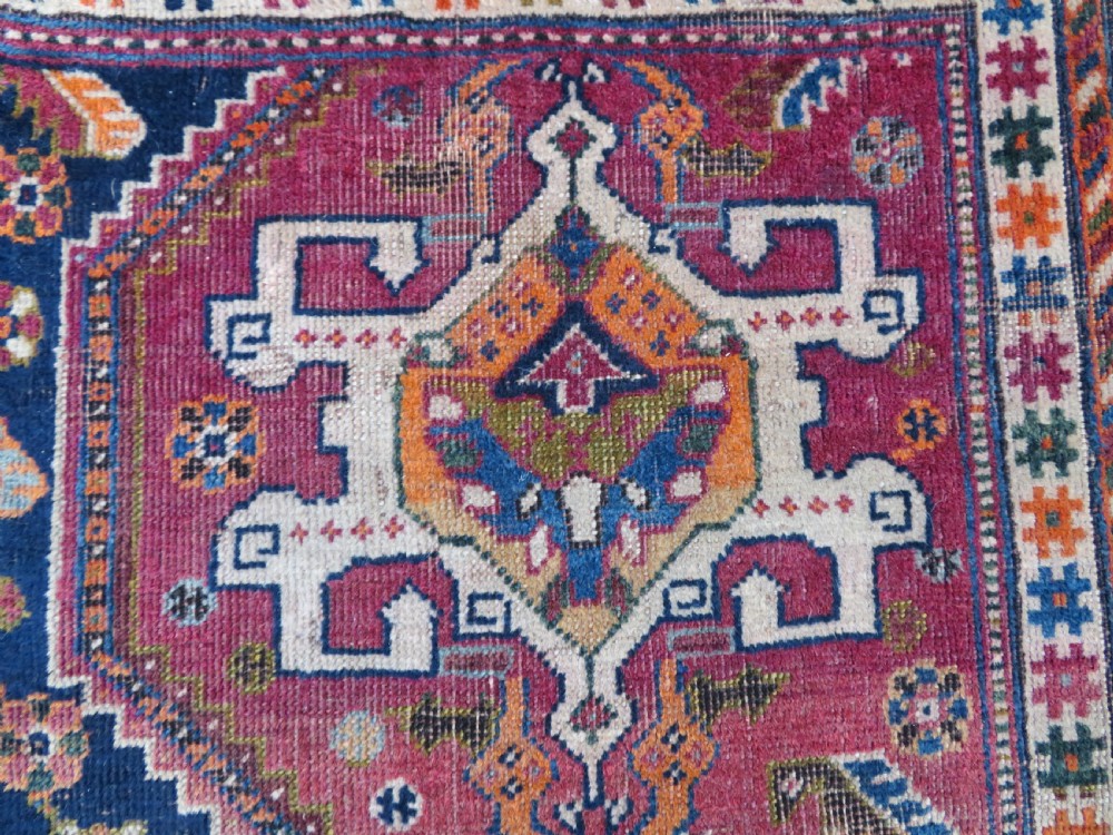 An antique Qashqai hand-knotted wool rug featuring a central diamond medallion surrounded by geometric tribal motifs in shades of navy blue, terracotta red, and cream. View VII