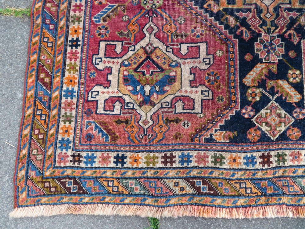 An antique Qashqai hand-knotted wool rug featuring a central diamond medallion surrounded by geometric tribal motifs in shades of navy blue, terracotta red, and cream. View VIII
