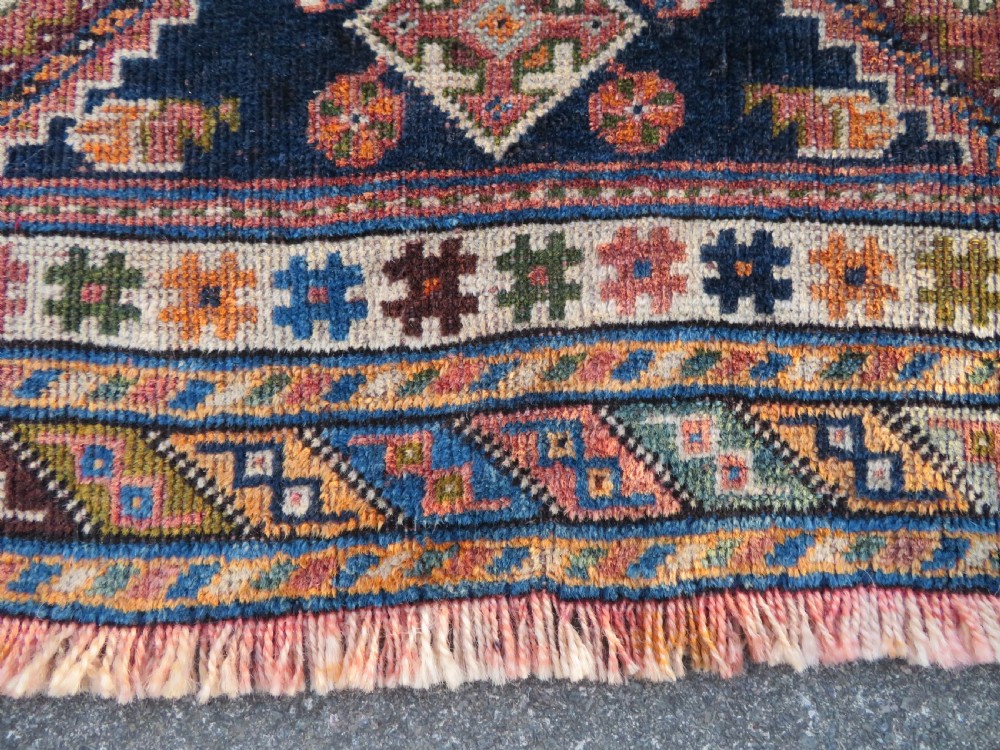 An antique Qashqai hand-knotted wool rug featuring a central diamond medallion surrounded by geometric tribal motifs in shades of navy blue, terracotta red, and cream. View IX